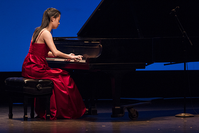 Photo of female pianist in performance in a flowing red dress against a luminous blue background