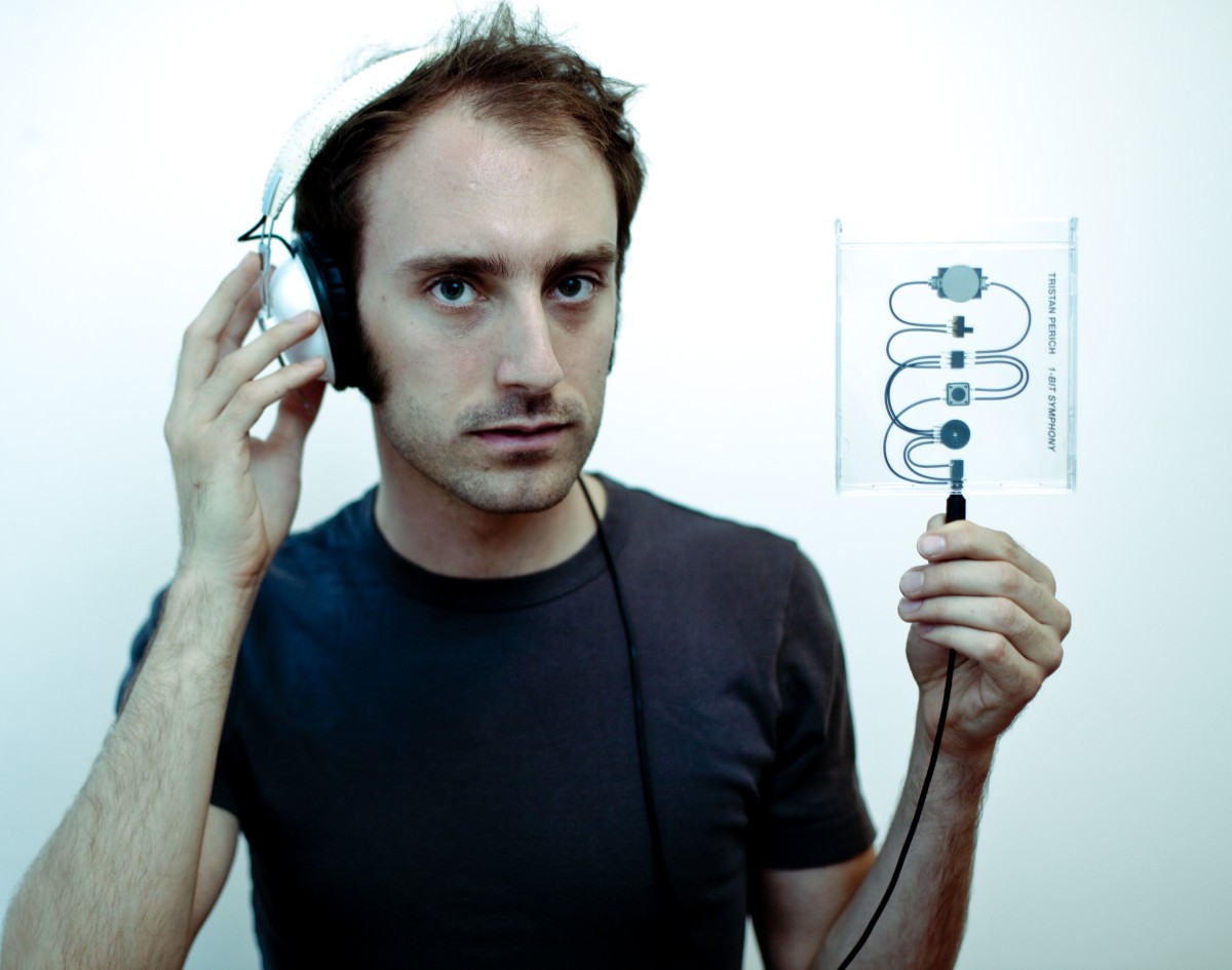 Photo of Tristan Preich with headphones holding up one of his one-bit instruments