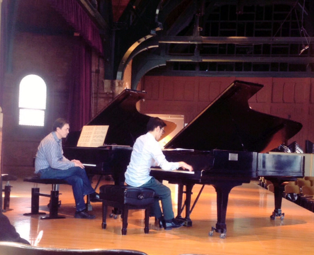 Photo of a masterclass on stage; pianist at right is playing while left watches on