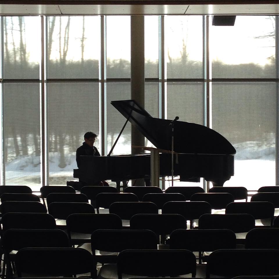 Moody photo of pianist playing against a snowy backdrop, visible through large windows, at the Lab of Ornithology